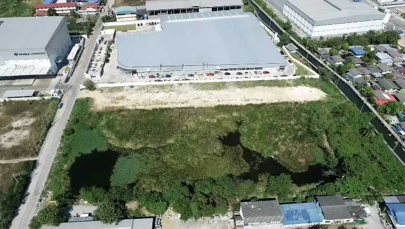 Aerial view of a warehouse next to a vacant, overgrown lot with standing water.