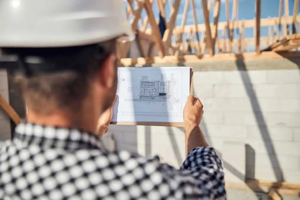 Construction worker in hard hat reviewing blueprints at a building site.